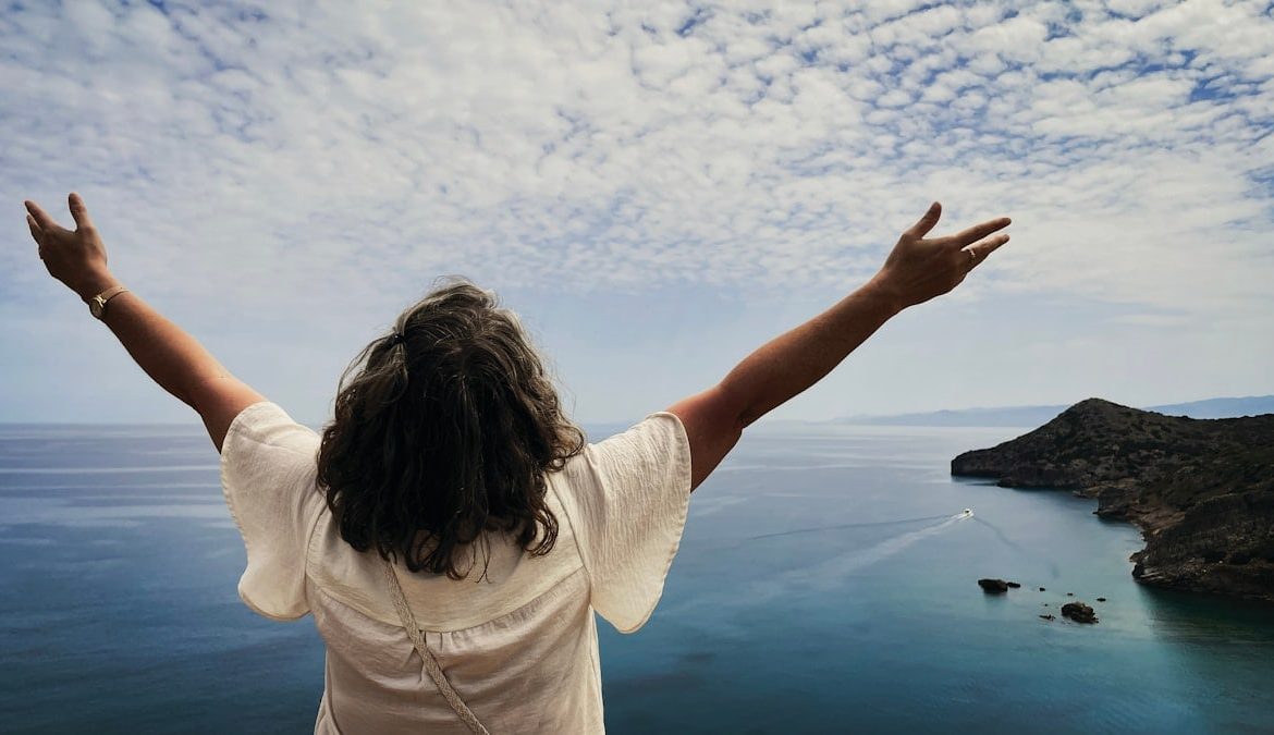 Woman with arms outstretched overlooking the ocean.